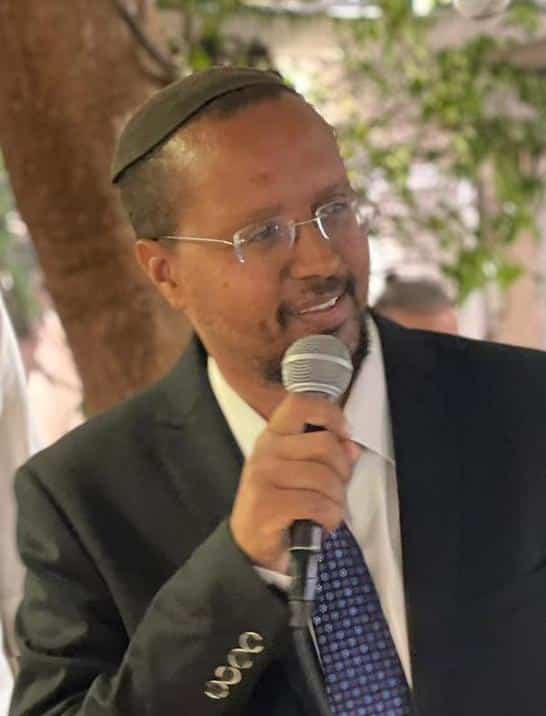 גבר מחייך בכיפה וחליפה מדבר למיקרופון.